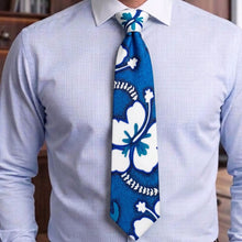 Load image into Gallery viewer, A men's necktie with a blue and white hibiscus floral pattern, worn with a light blue dress shirt.