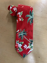 Load image into Gallery viewer, A red Hawaiian necktie with a tropical palm tree and hibiscus flower pattern, laid flat on a light wood surface.
