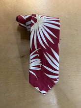 Load image into Gallery viewer, A necktie with a bold white palm leaf pattern on a deep burgundy background, laid flat on a light wood surface.
