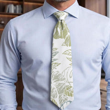 Load image into Gallery viewer, A men's necktie with a white base and light olive green tropical leaf pattern, worn with a light blue pinstriped dress shirt.
