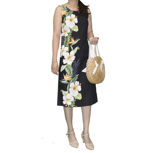 Woman wearing a black sleeveless dress with floral design, holding a straw bag on a white background
