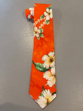 Load image into Gallery viewer, An orange necktie with a tropical floral print featuring white hibiscus flowers and green leaves, laid flat on a gray textured surface.
