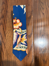 Load image into Gallery viewer, A navy blue necktie with a tropical floral print, laid flat on a dark wood surface.
