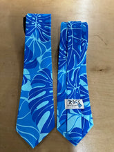 Load image into Gallery viewer, Two blue patterned neckties with a tropical leaf design, displayed side-by-side on a light wood surface. One tie shows a black neck strap, and the other features a white paper label with the brand name 'RY'S'.
