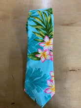 Load image into Gallery viewer, A tropical print necktie featuring pink and yellow plumeria flowers and green palm leaves on a light blue background, laid flat on a wooden surface.
