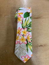 Load image into Gallery viewer, A white necktie featuring a tropical floral print with pink and yellow plumeria flowers and green leaves, laid flat on a light brown wooden surface.
