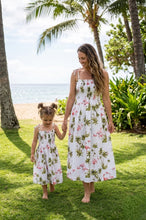 Load image into Gallery viewer, Woman and child in matching floral dresses standing on grass with palm trees and ocean in the background

