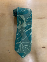 Load image into Gallery viewer, A teal and light green tropical leaf patterned necktie, laid flat on a light wood surface.
