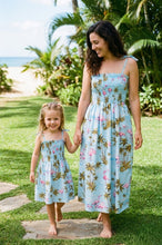 Load image into Gallery viewer, Woman and child in matching floral dresses standing on a grassy path with greenery and ocean in the background.
